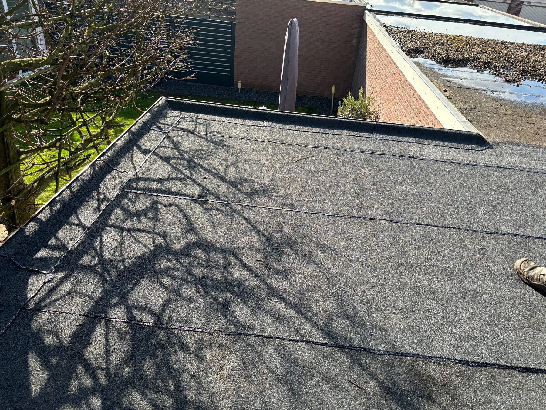 Nieuw aangebrachte bitumen toplaag op een plat dak achter een woning