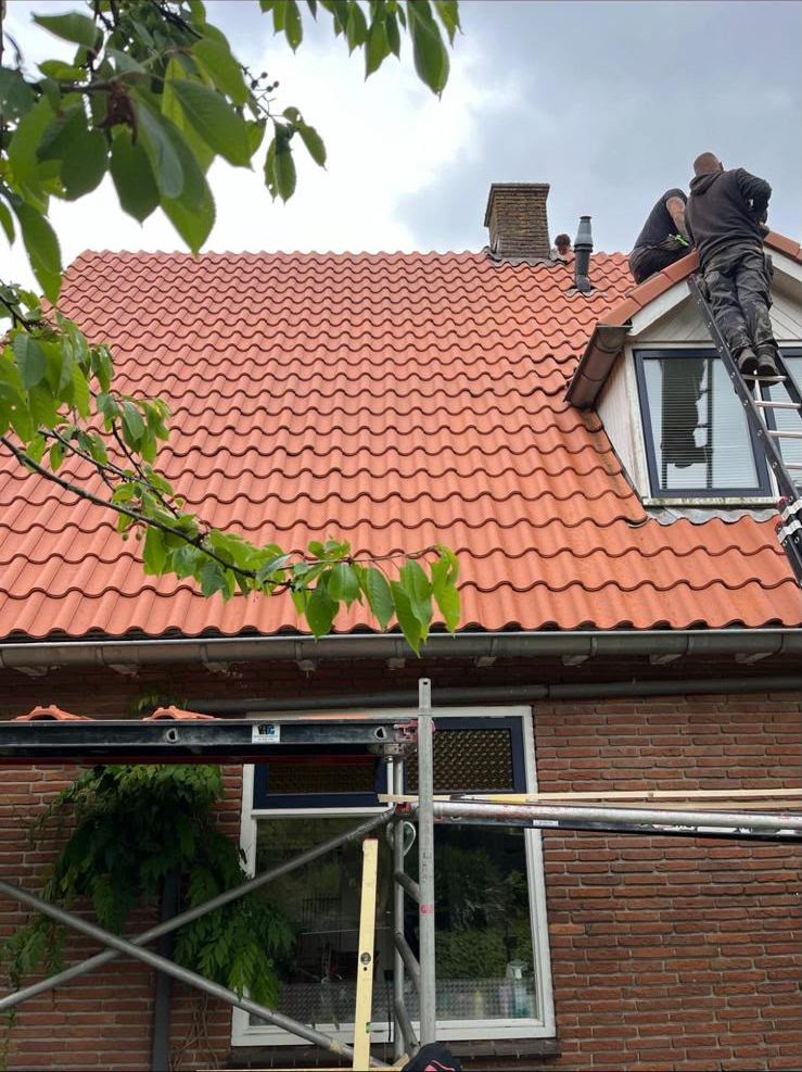 Dakdekkers werken aan de dakkapel van een oranje pannendak