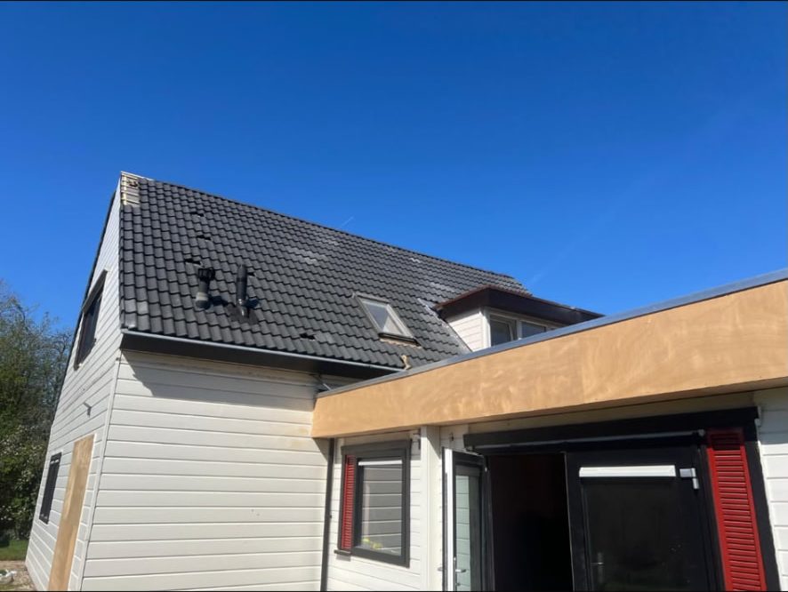 Woning met zwart pannendak en nieuw plat dak op de aanbouw